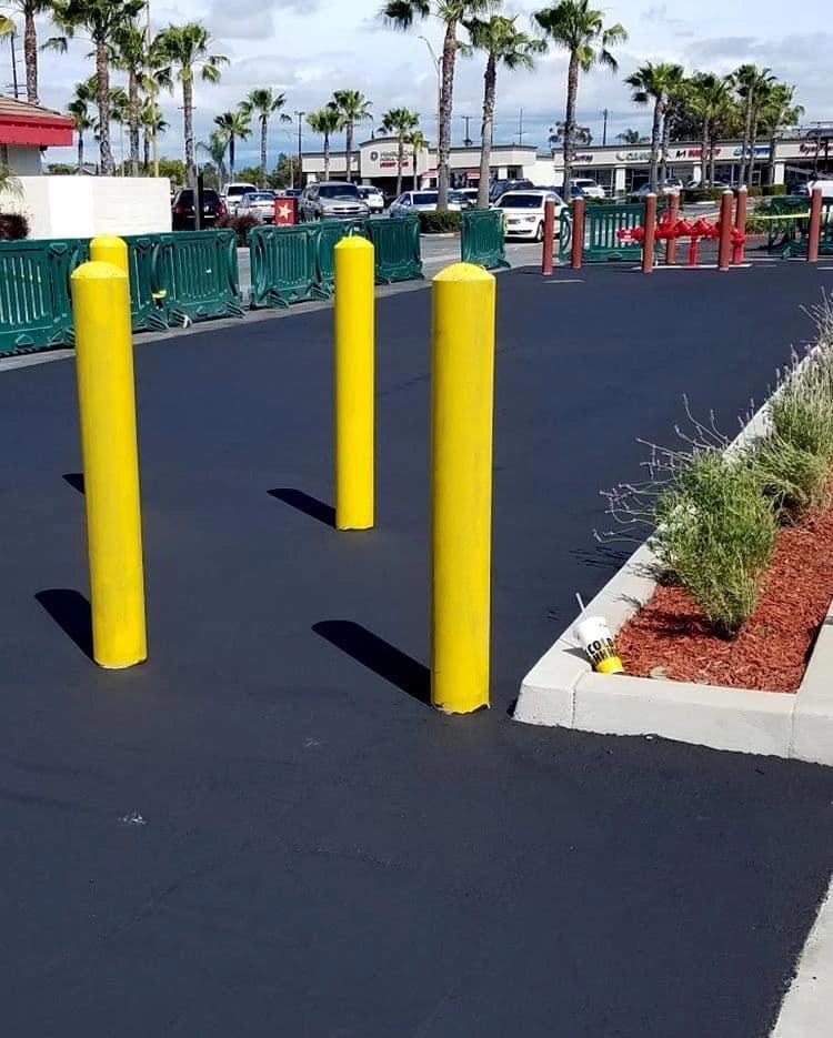 Yellow safety bollards set in freshly sealed asphalt beside a landscaped curb