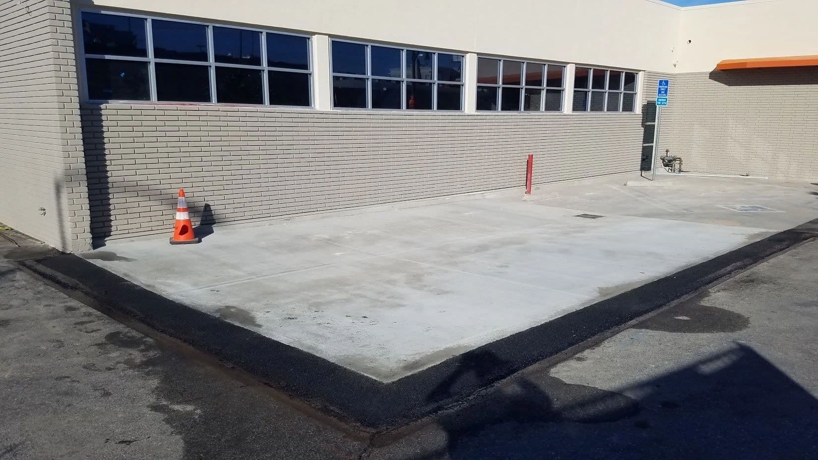 Newly poured concrete pad edged with fresh asphalt beside a commercial building