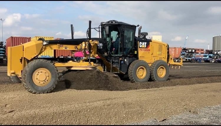 Caterpillar motor grader spreading and leveling base material across a large site