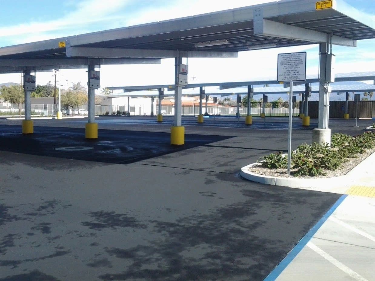 New asphalt beneath solar carports, with an accessible parking stall marked in blue next to a concrete curb