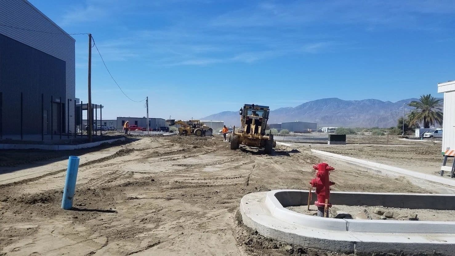 Motor grader working a dirt pad at a new development beside freshly poured curbs and a fire hydrant